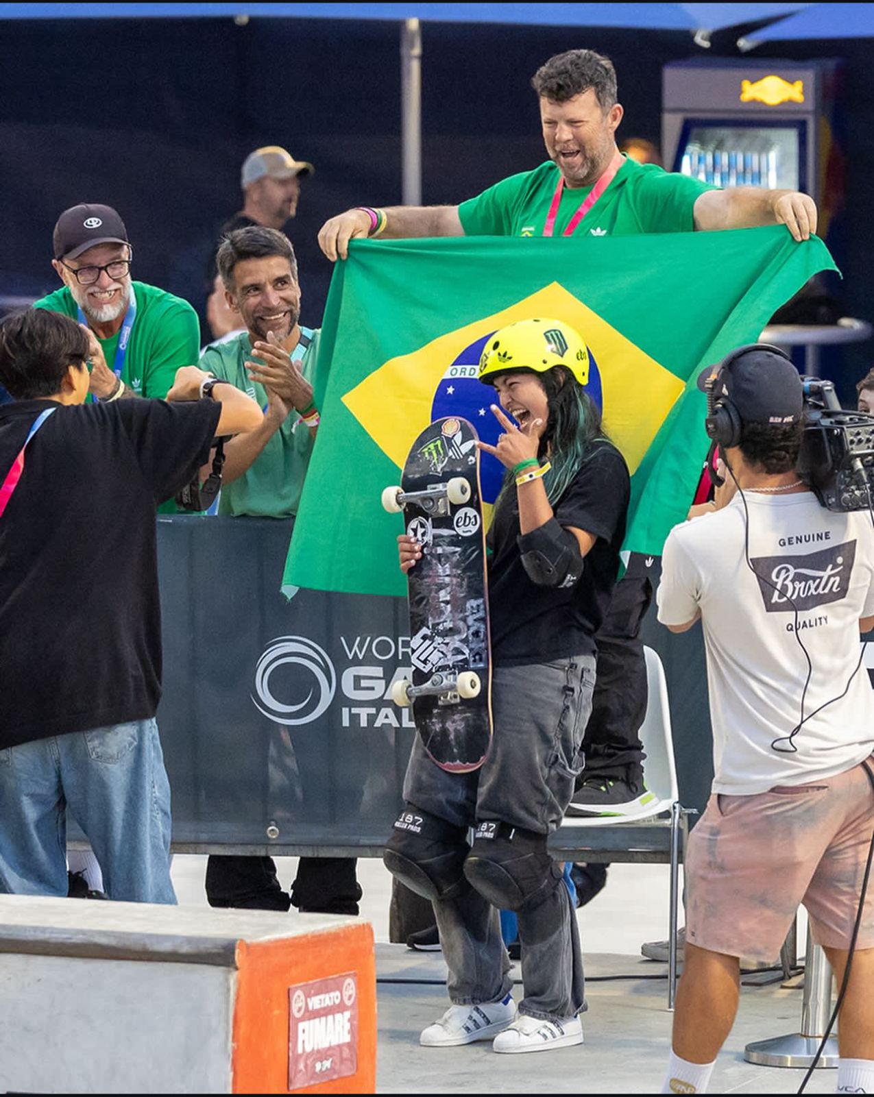 Imagem da skatista Raicca Ventura posando para foto em frente a bandeira do Brasil.