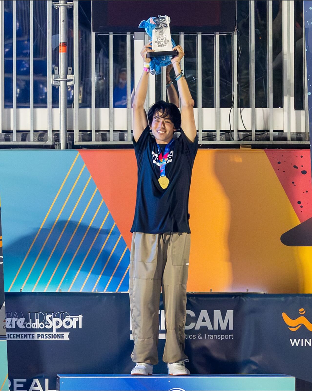 Imagem do skatista Augusto Akio no pódio segurando seu troféu de campeão.